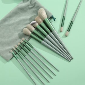 A 13-piece makeup brush set in a soft sage green color. The set includes various sizes of brushes with light beige, soft bristles and matte green handles. A matching green velvet drawstring storage pouch is shown in the corner. The brushes are arranged neatly on a solid light green background.