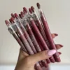 A hand with light pink nails holding a bundle of wooden makeup pencils. The pencils are Flormar Matte Color Lipsticks in a variety of nude, mauve, and deep berry shades. Each pencil has a clear plastic cap, and several of the caps feature a convenient built-in sharpener.